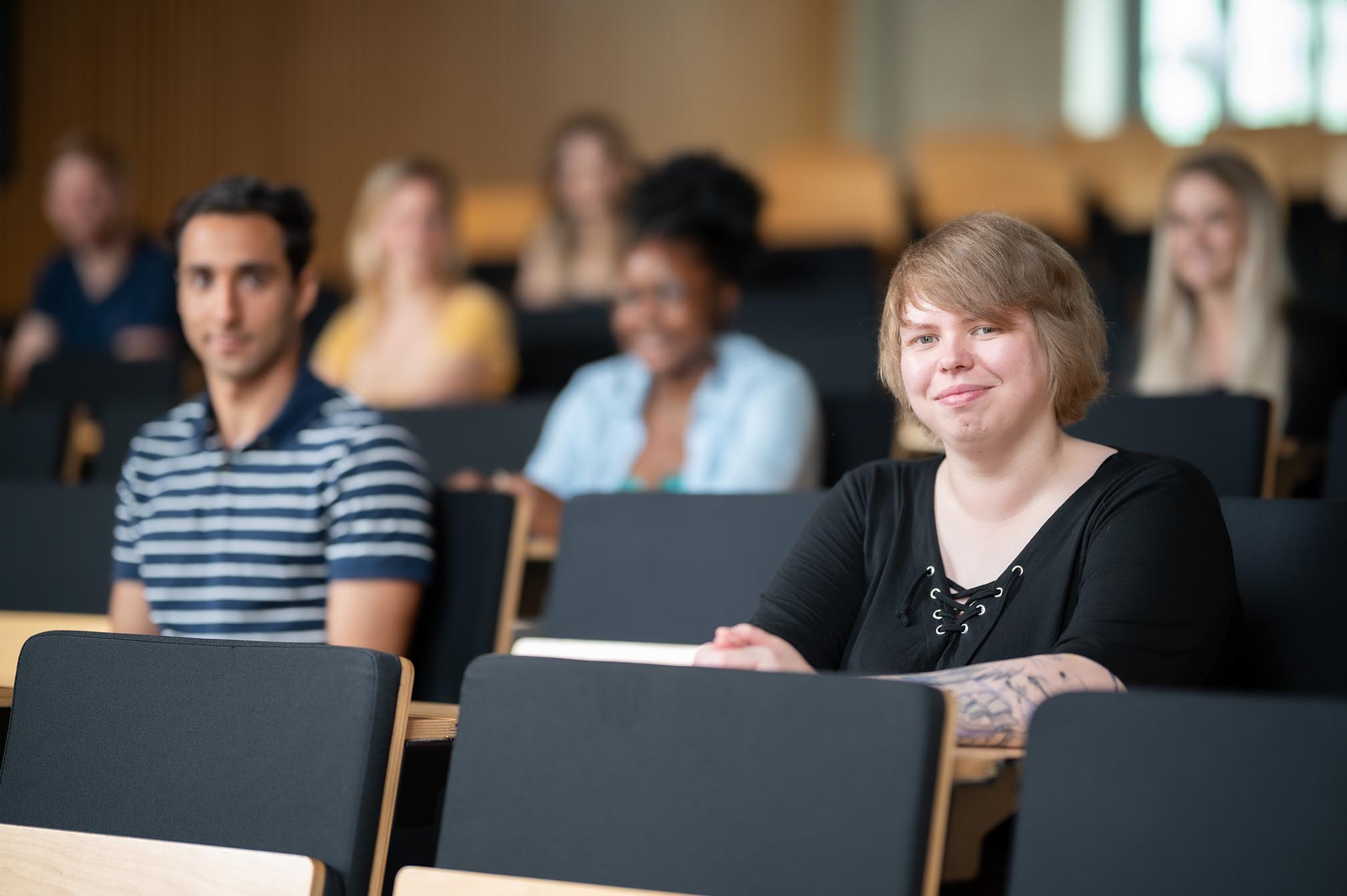 Eine Studentin sitzt in einem Hörsaal mit einer Gruppe von Studierenden im Hintergrund auf dem Campus Bottrop.