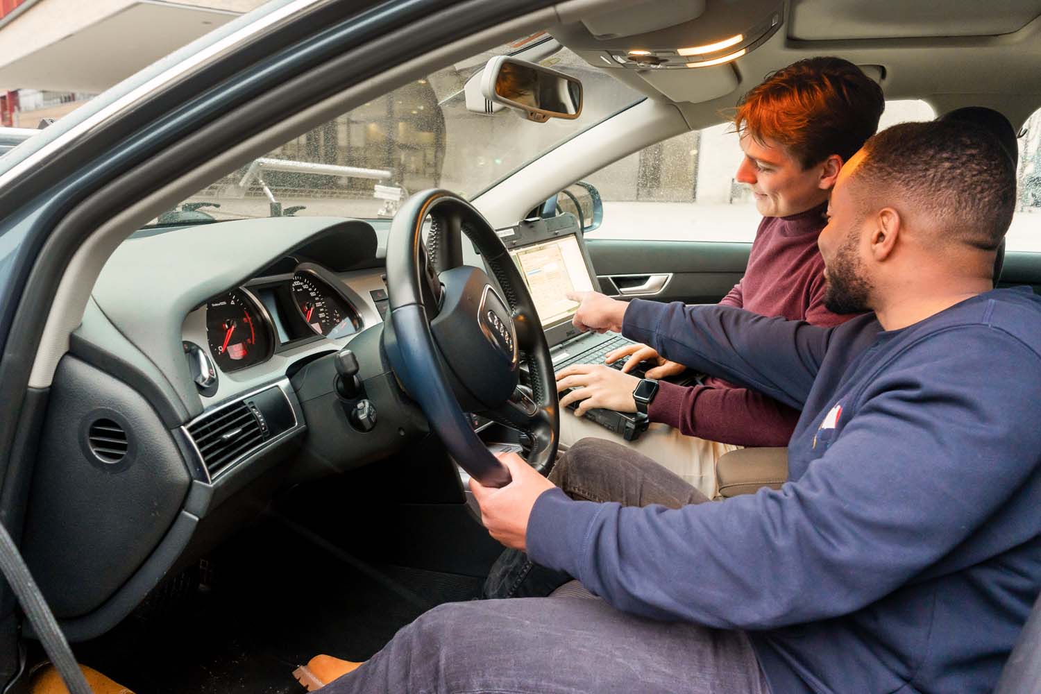 Zwei Studenten sitzen im Auto, halten einen Laptop und besprechen Daten, die vom Autocomputer exportiert wurden.